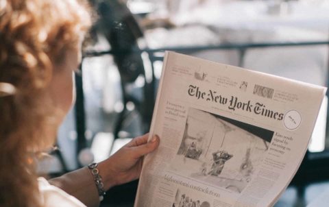 A woman sitting and reading a copy of The New York Times newspaper