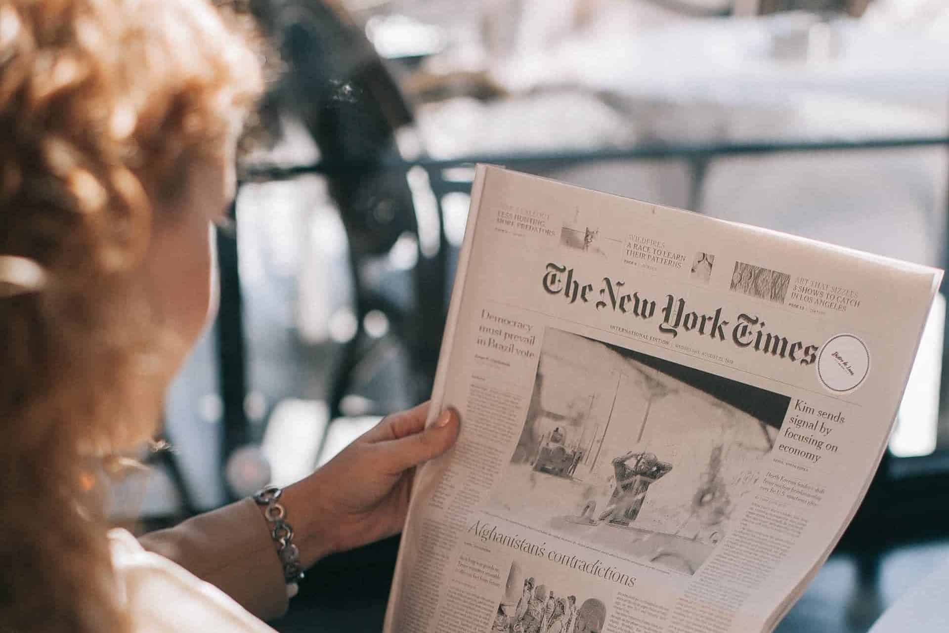 A woman sitting and reading a copy of The New York Times newspaper