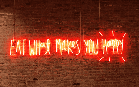 Eat What Makes You Happy in red neon lights on a brick wall
